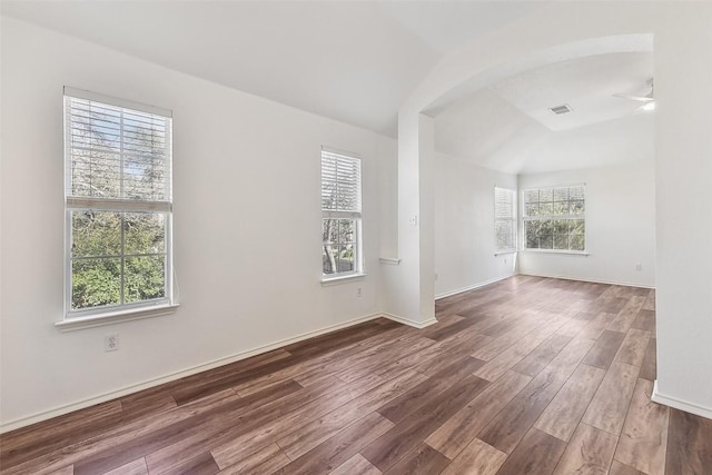 empty room with baseboards, visible vents, a ceiling fan, arched walkways, and wood finished floors