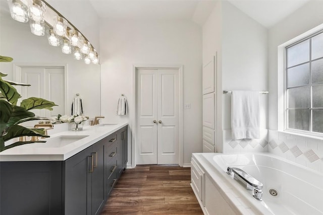 bathroom featuring a washtub, vanity, wood-type flooring, and vaulted ceiling