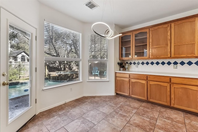 interior space featuring brown cabinets, tasteful backsplash, glass insert cabinets, and visible vents