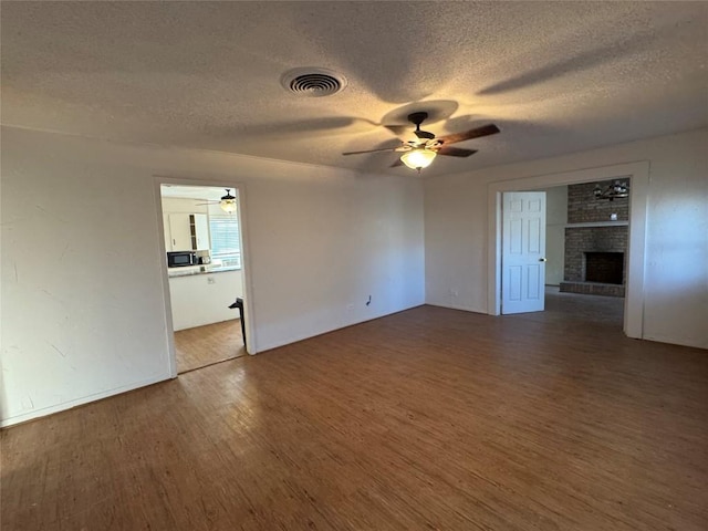 unfurnished room with hardwood / wood-style flooring, a fireplace, a textured ceiling, and ceiling fan