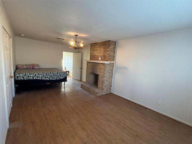 unfurnished bedroom with dark wood-type flooring, an inviting chandelier, a brick fireplace, and a textured ceiling