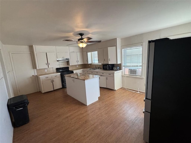 kitchen with white cabinetry, black appliances, light hardwood / wood-style floors, and a kitchen island