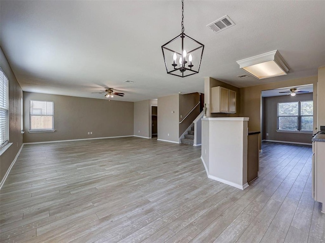 unfurnished living room with light hardwood / wood-style flooring, ceiling fan with notable chandelier, and a wealth of natural light