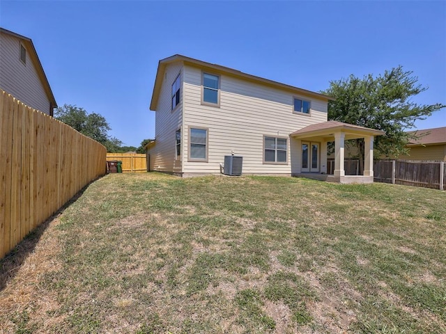 back of property with central AC unit and a yard