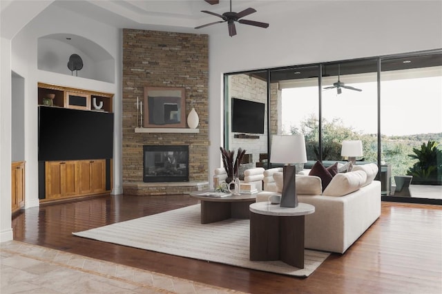 living room featuring a high ceiling, hardwood / wood-style floors, a fireplace, and ceiling fan