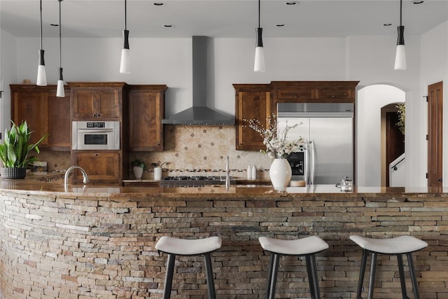 kitchen with tasteful backsplash, stainless steel appliances, a breakfast bar area, and wall chimney range hood