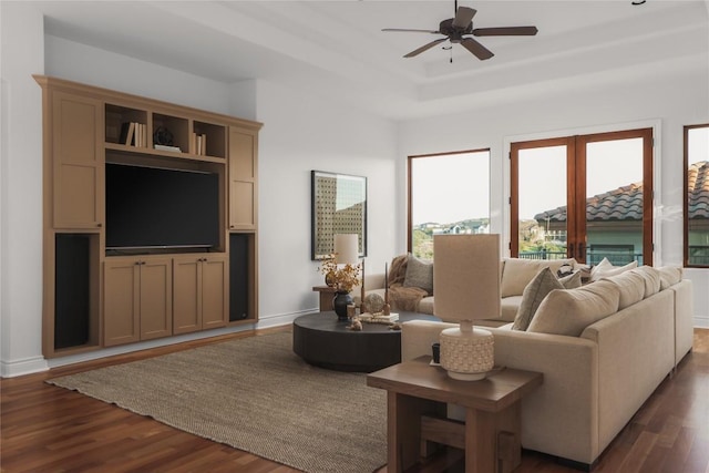 living room with a tray ceiling, dark wood-type flooring, and ceiling fan