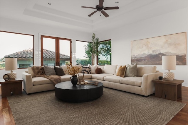 living room featuring dark hardwood / wood-style floors, a raised ceiling, and ceiling fan