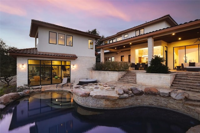 back house at dusk featuring ceiling fan and a patio area