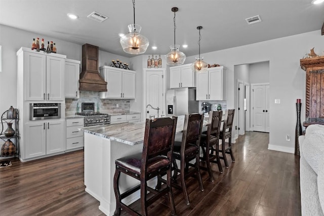 kitchen featuring white cabinetry, premium range hood, appliances with stainless steel finishes, and a center island with sink