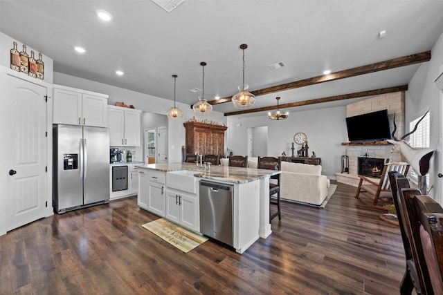 kitchen with white cabinetry, light stone counters, hanging light fixtures, a center island with sink, and appliances with stainless steel finishes