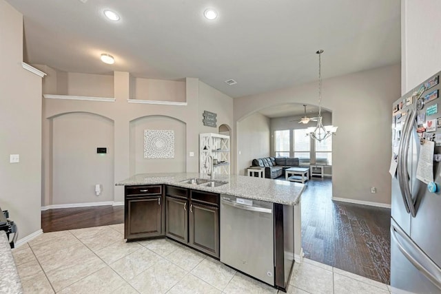 kitchen with appliances with stainless steel finishes, decorative light fixtures, sink, light stone counters, and dark brown cabinets