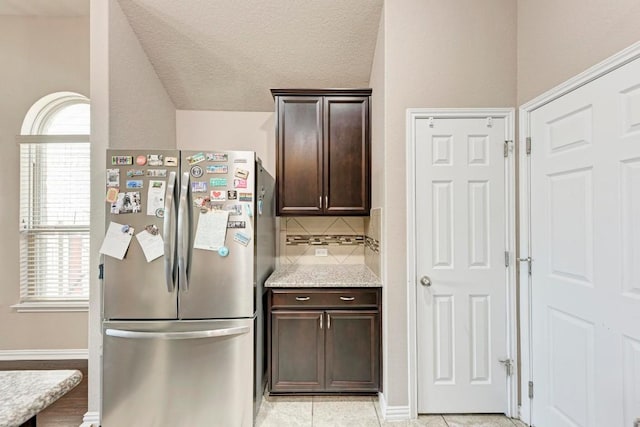 kitchen with tasteful backsplash, light stone countertops, stainless steel fridge, and dark brown cabinetry