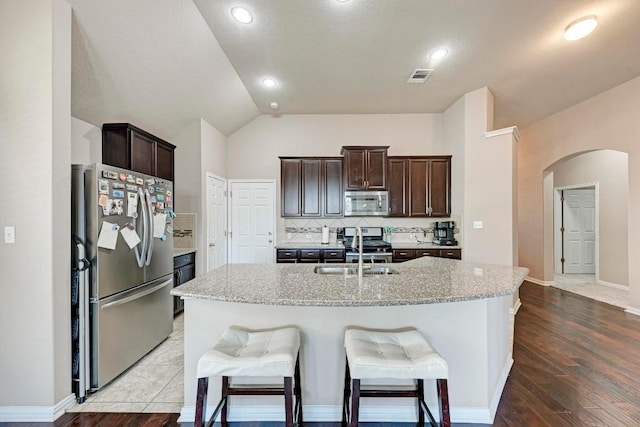 kitchen with light stone counters, an island with sink, appliances with stainless steel finishes, and sink