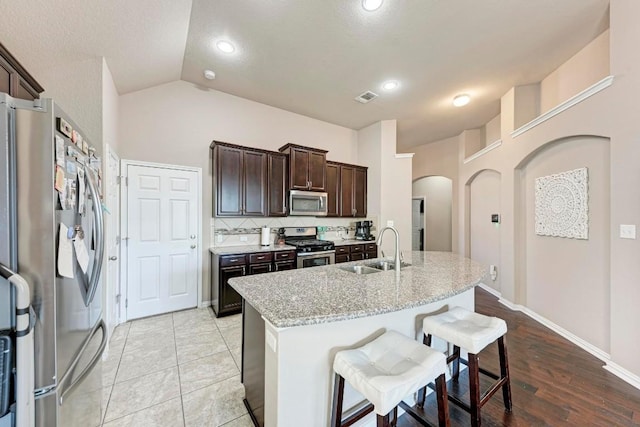 kitchen with a breakfast bar, sink, an island with sink, stainless steel appliances, and light stone countertops