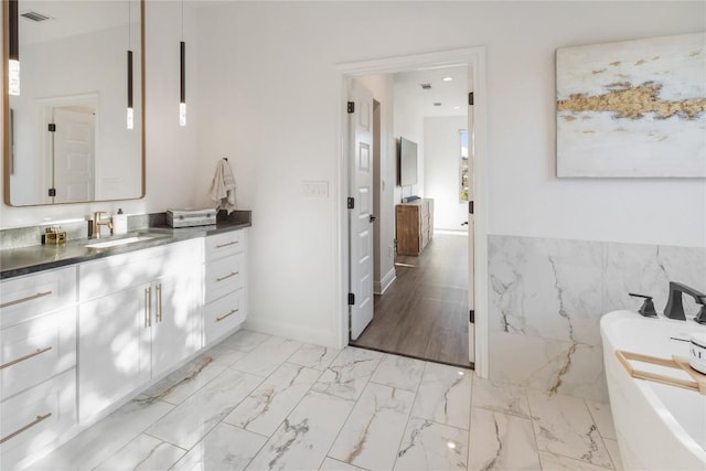 full bathroom with marble finish floor, a freestanding tub, tile walls, and vanity