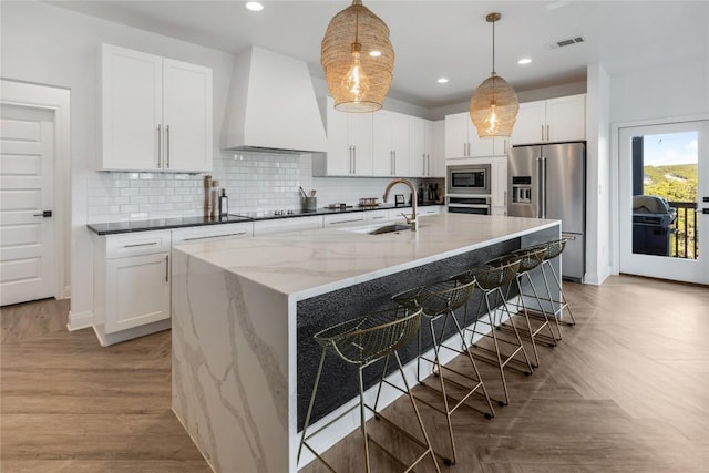 kitchen featuring visible vents, appliances with stainless steel finishes, dark stone countertops, custom exhaust hood, and a sink