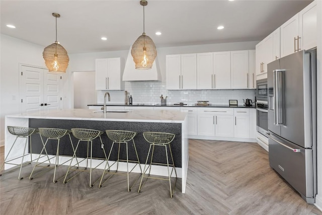 kitchen with a kitchen island with sink, a sink, white cabinetry, hanging light fixtures, and appliances with stainless steel finishes