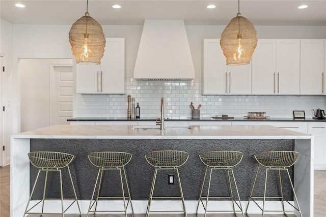 kitchen featuring a breakfast bar, premium range hood, and white cabinetry