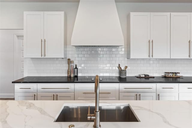 kitchen with black electric stovetop, a sink, white cabinets, and custom range hood