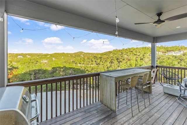 wooden terrace with a bar, a wooded view, and a ceiling fan