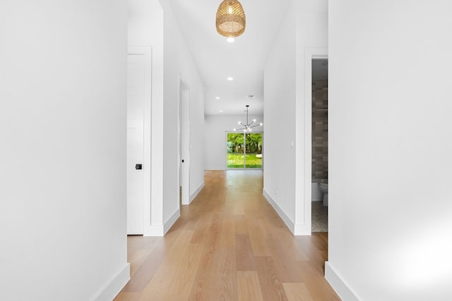 corridor featuring light wood-type flooring and a notable chandelier