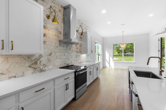 kitchen featuring pendant lighting, sink, white cabinets, stainless steel appliances, and wall chimney exhaust hood