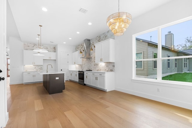 kitchen with wall chimney exhaust hood, decorative light fixtures, an island with sink, and electric range