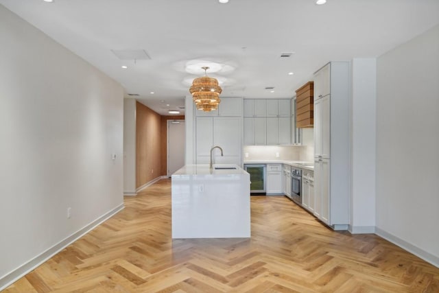 kitchen featuring wine cooler, sink, hanging light fixtures, a center island with sink, and light parquet floors