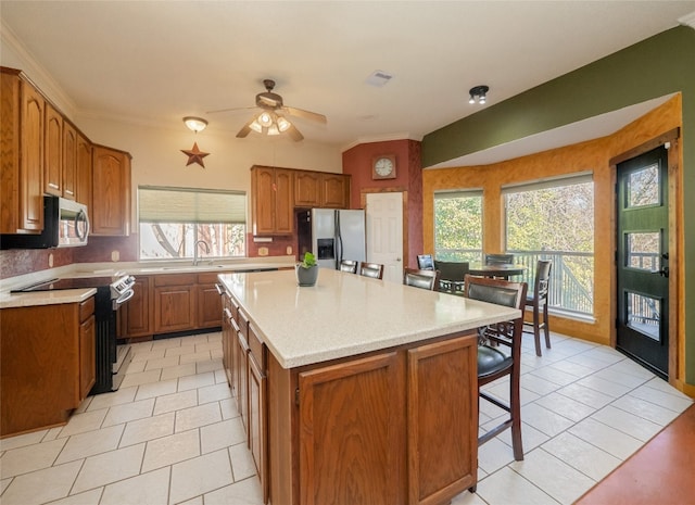 kitchen with a kitchen island, ornamental molding, appliances with stainless steel finishes, and light tile patterned floors