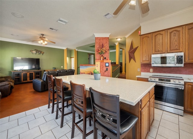 kitchen featuring crown molding, stainless steel appliances, a center island, and light tile patterned flooring