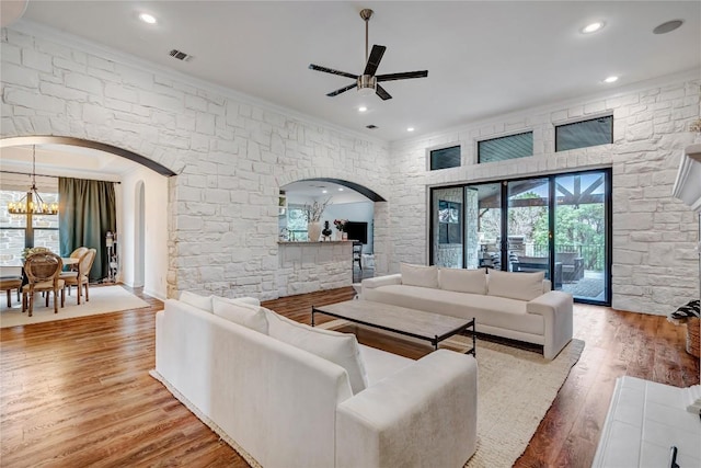 living room featuring ceiling fan with notable chandelier, wood-type flooring, and ornamental molding