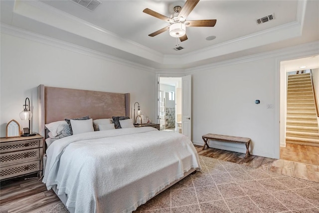 bedroom with ensuite bathroom, hardwood / wood-style flooring, ceiling fan, a raised ceiling, and crown molding