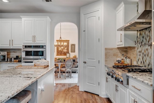 kitchen featuring white cabinetry, appliances with stainless steel finishes, light stone counters, and wall chimney range hood