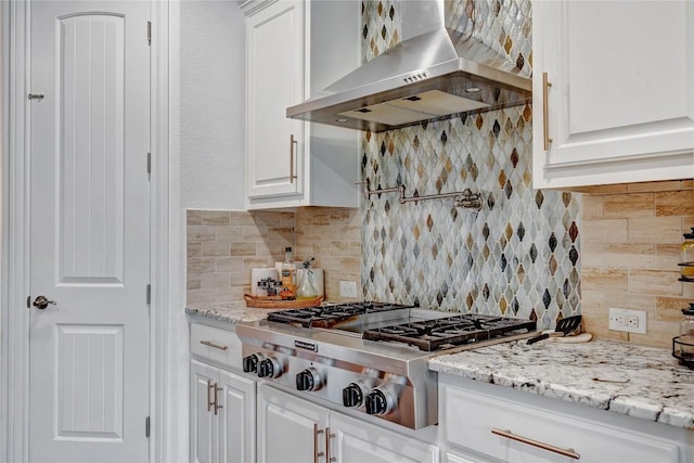 kitchen with stainless steel gas stovetop, tasteful backsplash, wall chimney range hood, and white cabinets