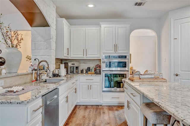 kitchen with sink, light stone counters, light wood-type flooring, appliances with stainless steel finishes, and white cabinets