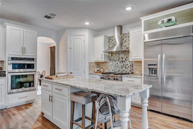 kitchen with white cabinetry, appliances with stainless steel finishes, light stone countertops, and wall chimney range hood