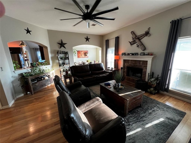 living room with hardwood / wood-style flooring, ceiling fan, and a brick fireplace