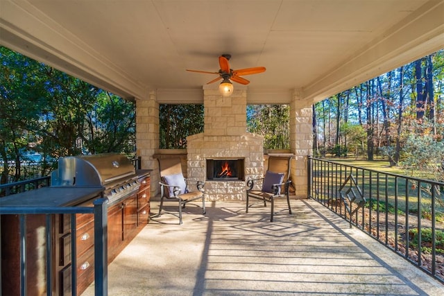 wooden terrace featuring exterior kitchen, ceiling fan, grilling area, and an outdoor stone fireplace