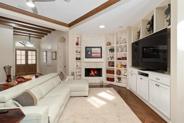 living room featuring a stone fireplace, dark hardwood / wood-style floors, built in features, beamed ceiling, and ornamental molding