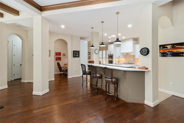 kitchen featuring decorative light fixtures, tasteful backsplash, white cabinetry, dark hardwood / wood-style flooring, and a kitchen bar