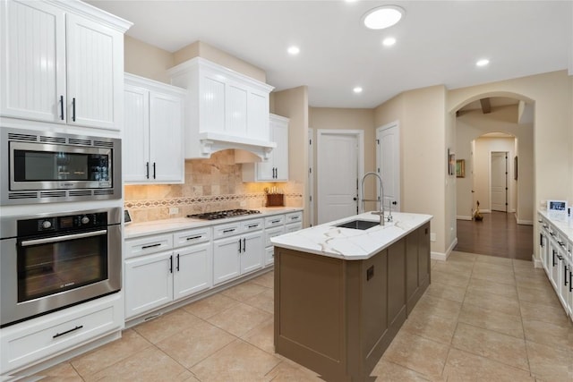 kitchen with sink, white cabinetry, stainless steel appliances, light stone countertops, and an island with sink