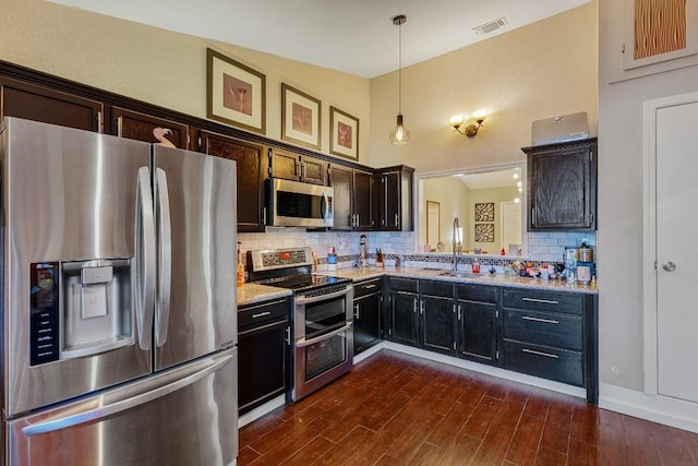 kitchen featuring sink, tasteful backsplash, light stone counters, decorative light fixtures, and appliances with stainless steel finishes