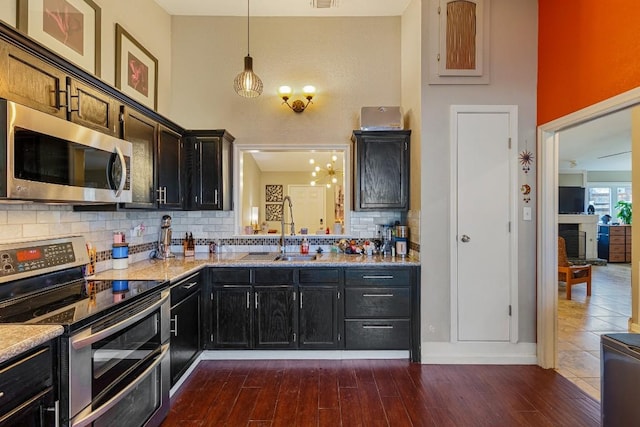 kitchen with appliances with stainless steel finishes, sink, pendant lighting, and light stone counters