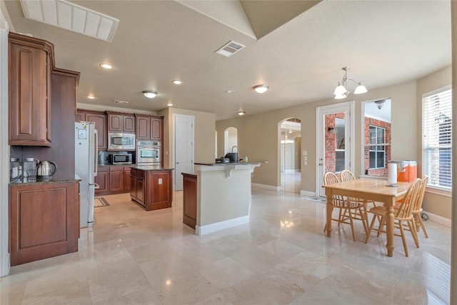 kitchen featuring a kitchen island, stainless steel microwave, decorative light fixtures, a chandelier, and fridge