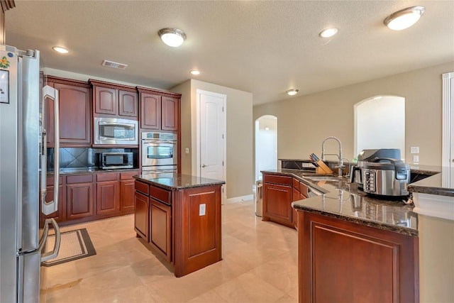 kitchen featuring stainless steel appliances, a center island, sink, and dark stone countertops