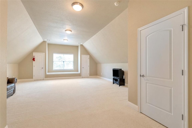 additional living space featuring light colored carpet, vaulted ceiling, and a textured ceiling