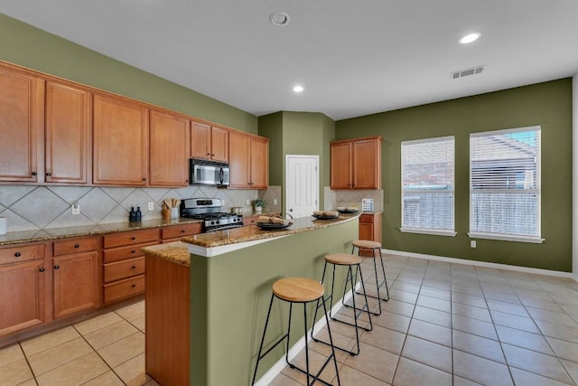 kitchen with a kitchen island, a breakfast bar, decorative backsplash, light stone counters, and stainless steel appliances