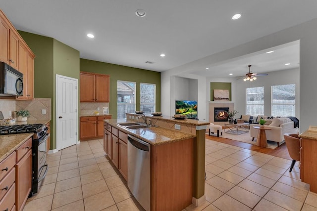 kitchen with light tile patterned floors, a tiled fireplace, sink, and black appliances