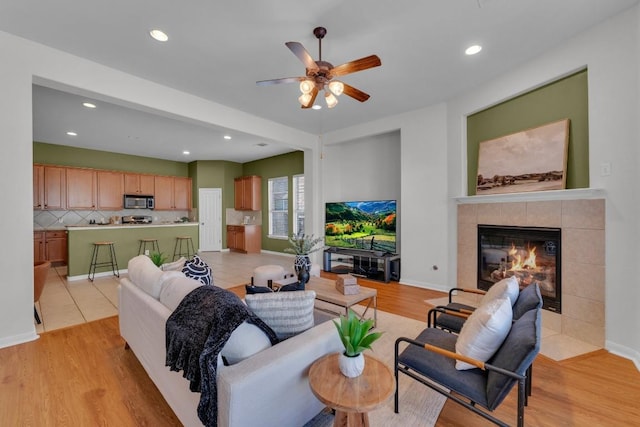 living room featuring a tiled fireplace, ceiling fan, and light hardwood / wood-style floors